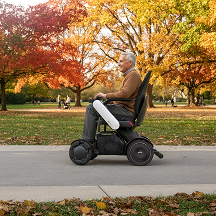 Man using a WHILL Model C2 highback in a park with autumn trees
