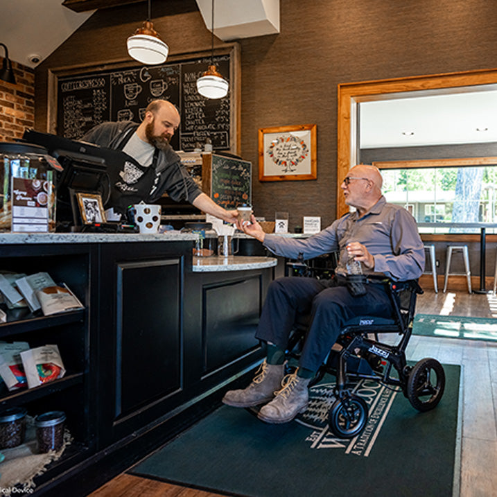 Person in a Pride Jazzy Ultra Light Power Chair receiving a drink at a cafe counter.
