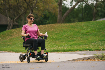Woman using a mobility scooter on a sidewalk with grass and trees in the background