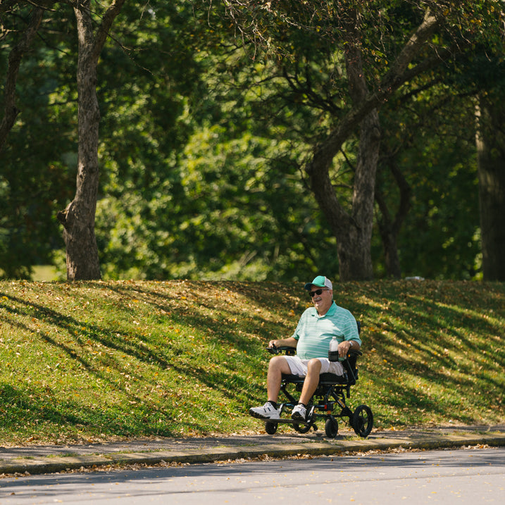 Man in a Jazzy carbon HD on a path in a park with trees in the background
