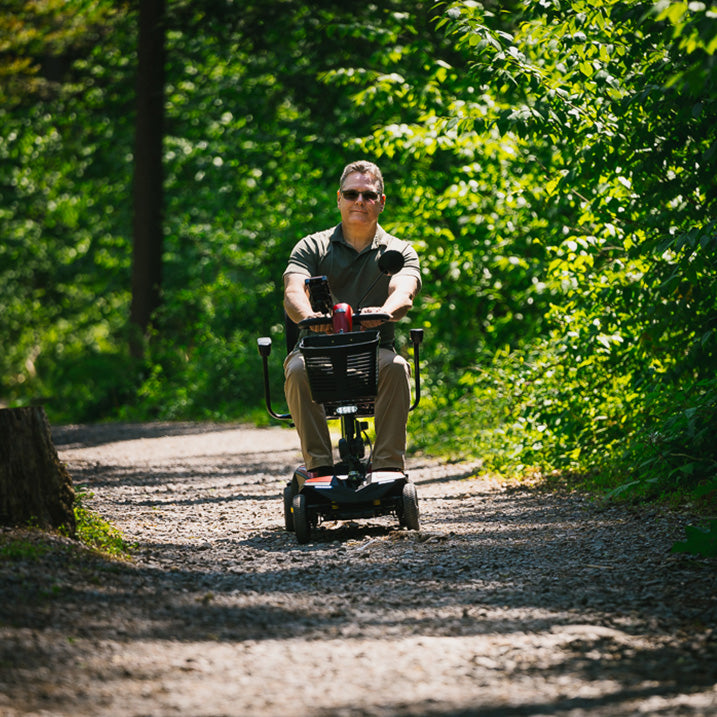 Man riding a Pride Go-Go Endurance AL+ scooter  on a trail surrounded by greenery