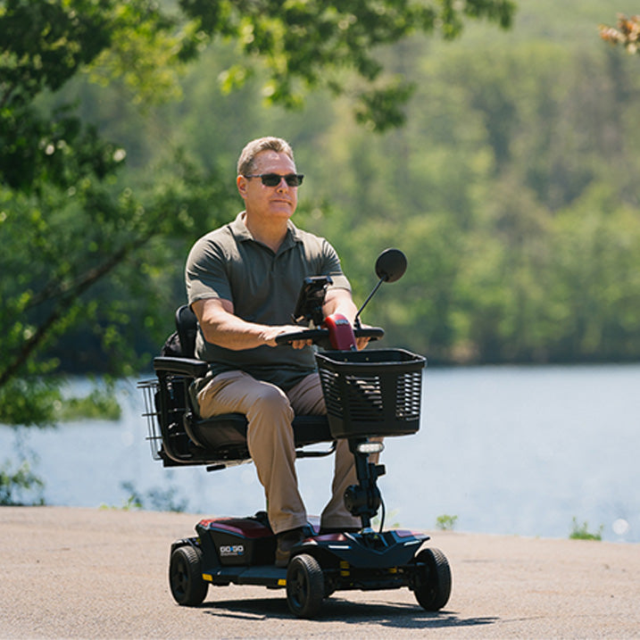 Man riding a Pride Go-Go Endurance AL+ scooter Black and Red by a lake with trees in the background