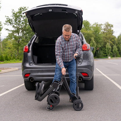 Man loading a  pride go go carbon scooter into the trunk of a car in a parking lot.