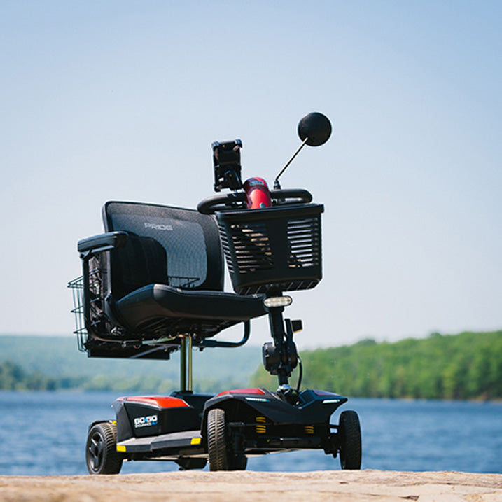 Pride Go-Go Endurance AL+ scooter  scooter with red accents on a wooden platform by a lake