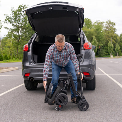 Man unloading a folded  pride go go carbon scooter from the trunk of a car in a parking lot.