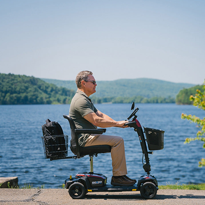 Man using a mobility scooter by a lake with mountains in the background