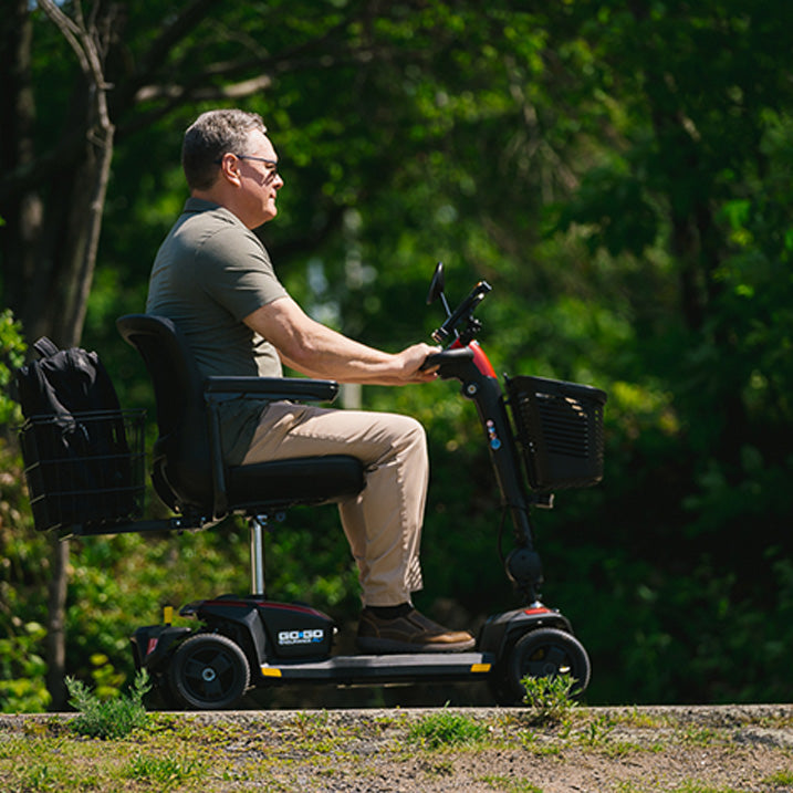 Man using a mobility scooter in a park-like setting with greenery.