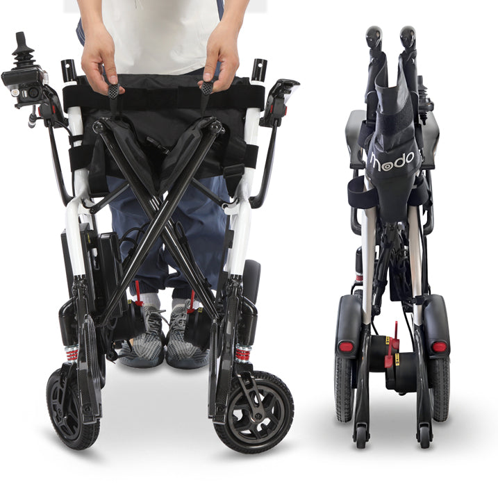 A compact Modo Breeze Ultralightweight Folding Electric Wheelchair shown in two views on a white background: one with a person's hands and lower body visible adjusting the seat area, and one folded view showing the product's compact folded dimensions. The wheelchair has a black and white frame with black wheels, black seat and backrest, and small red reflectors.