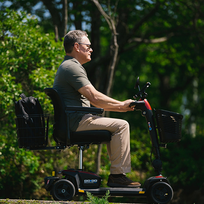 Man riding a mobility scooter in a park-like setting with trees in the background