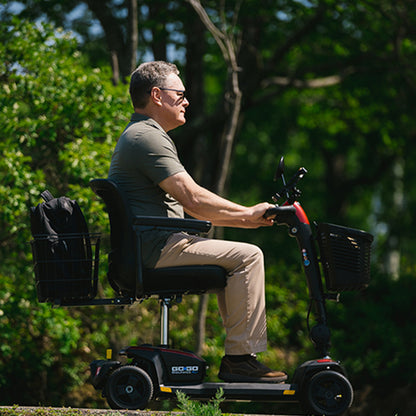 Man riding a mobility scooter in a park-like setting with trees in the background
