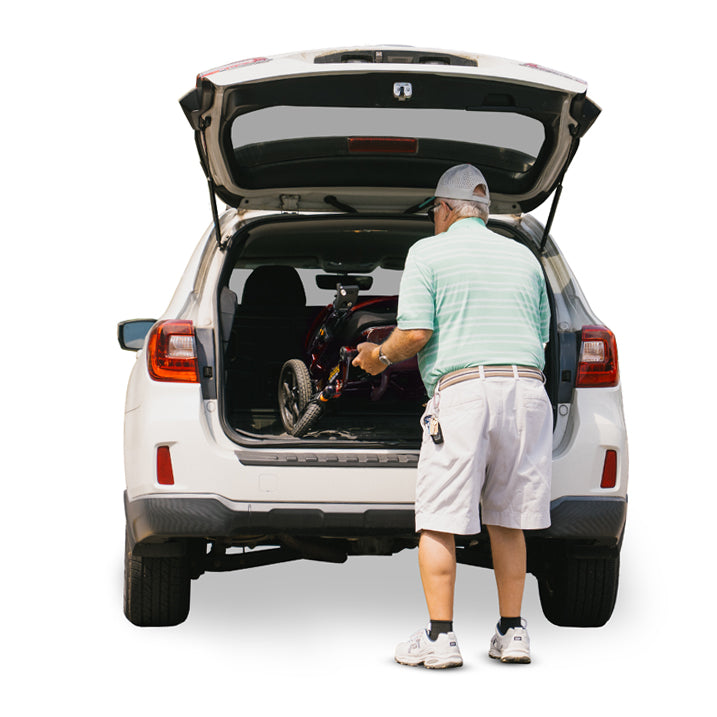 Man loading jazzy carbon HD into the trunk of a white SUV on a white background