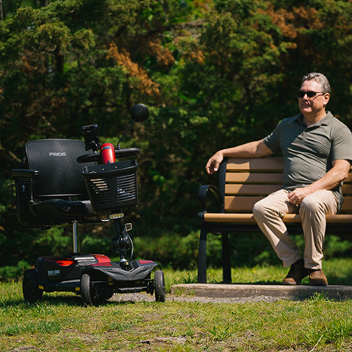Man sitting on a bench next to a mobility scooter in a park setting