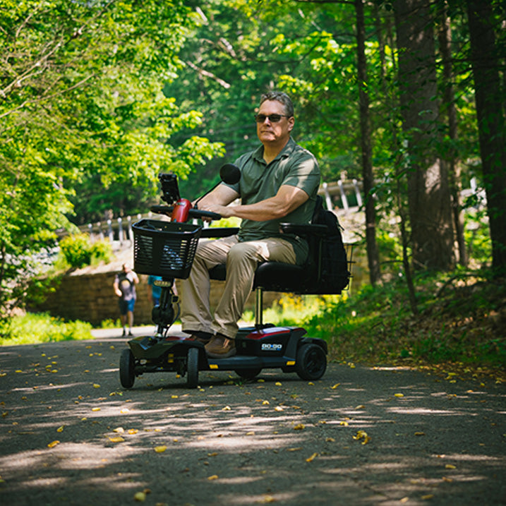 Man using a mobility scooter in a park with trees and a path.