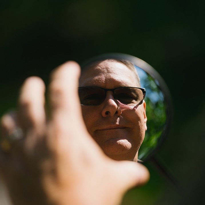 Person holding a round mirror reflecting their face outdoors