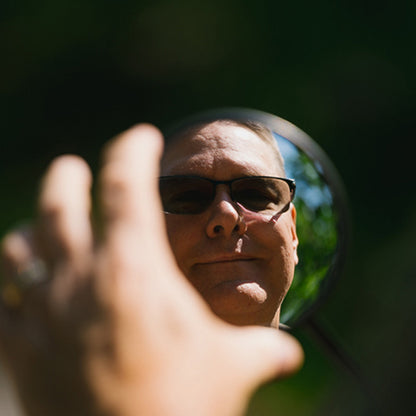 Person holding a round mirror reflecting their face outdoors