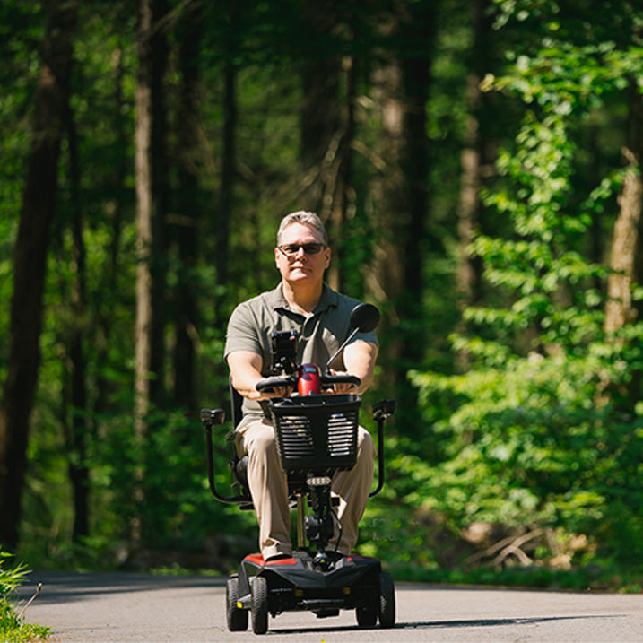Man riding a mobility scooter on a path surrounded by trees