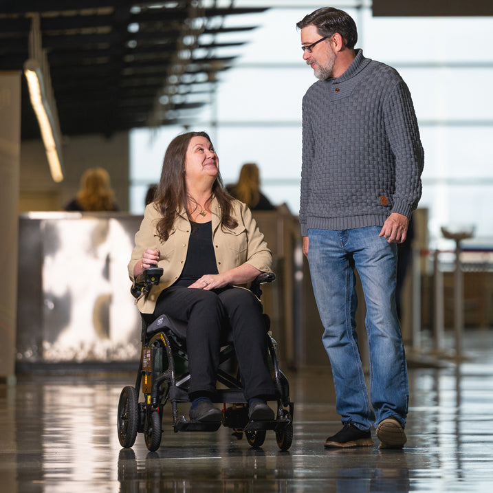 Woman in a wheelchair being pushed by a man in an indoor setting