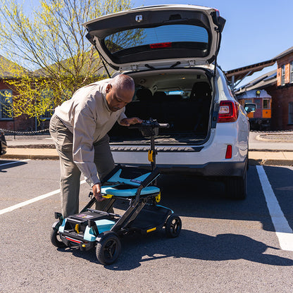 Man loading a pride go go super portable mobility scooter into the trunk of a car on a sunny day.