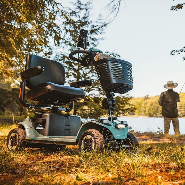 Pride Baja Bandit scooter with basket in a natural setting, person fishing in the background