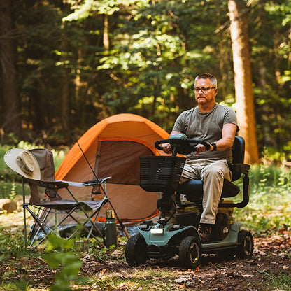 Man on a pride baja bandit scooter near an orange tent in a forest setting