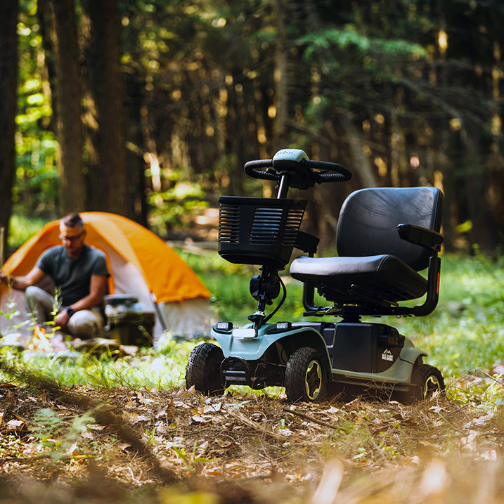 Pride Baja bandit scooter in a forest setting with a person sitting near an orange tent.