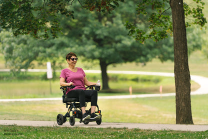 Person using a mobility scooter in a park setting with trees and grass.