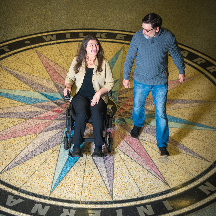 Two people, one in a wheelchair, standing on a decorative floor with compass design.