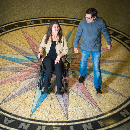 Two people, one in a wheelchair, standing on a decorative floor with compass design.