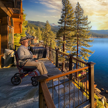 Person in a Jazzy carbon HD on a deck overlooking a scenic lake with trees and mountains.