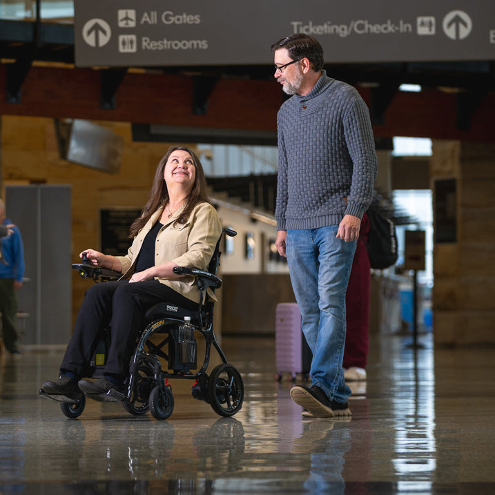 Woman in a wheelchair being pushed by a man in an airport terminal.